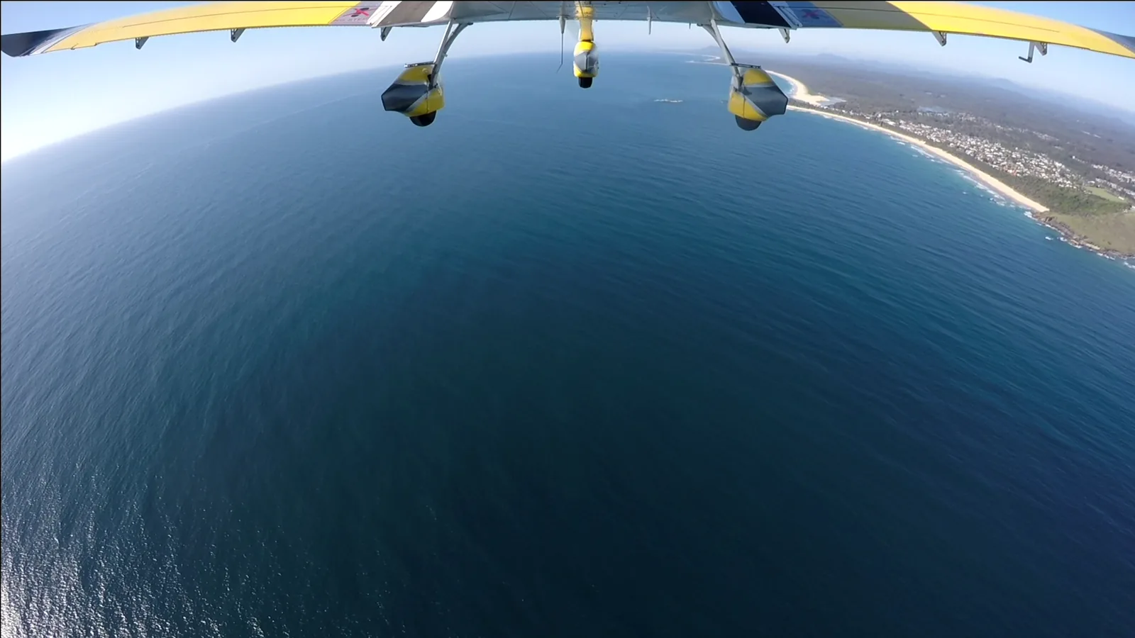 Blue water and coastline below an aircraft wing